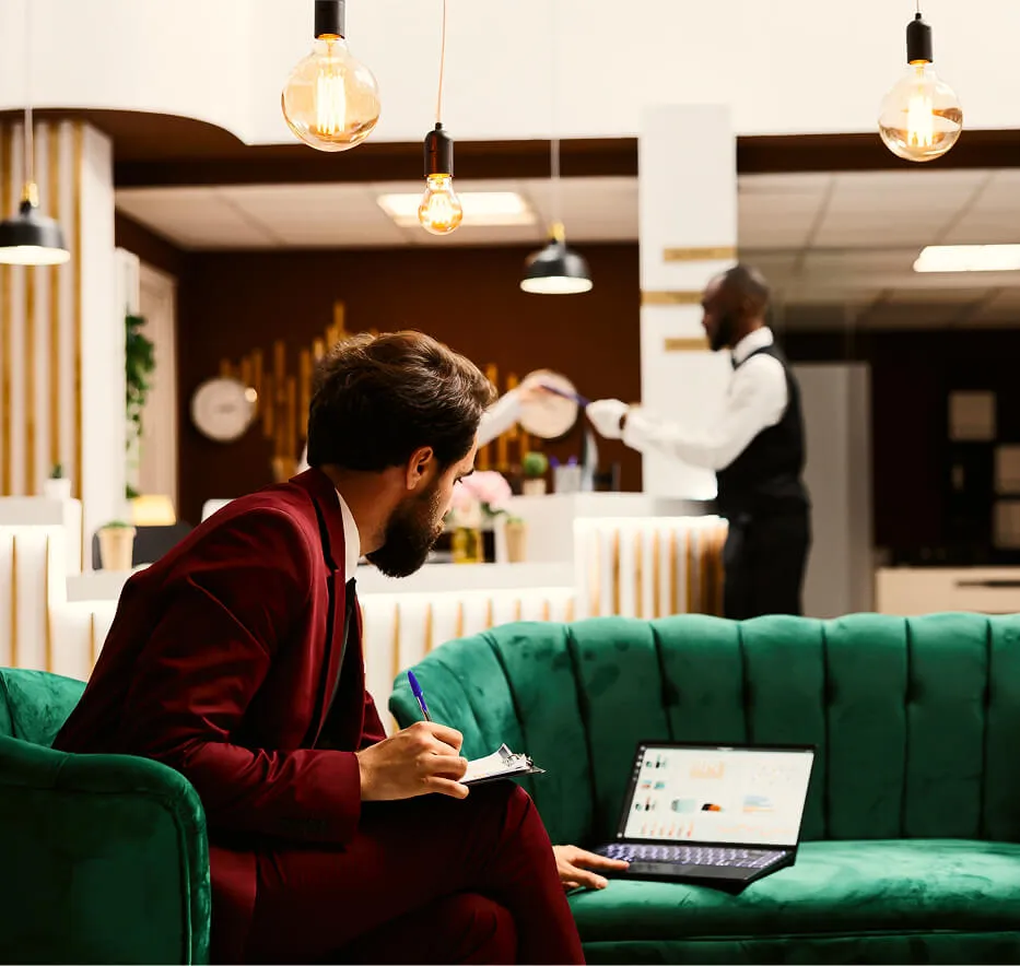 Man in red velvet suit tiping on notebook on green couch in hotel lobby