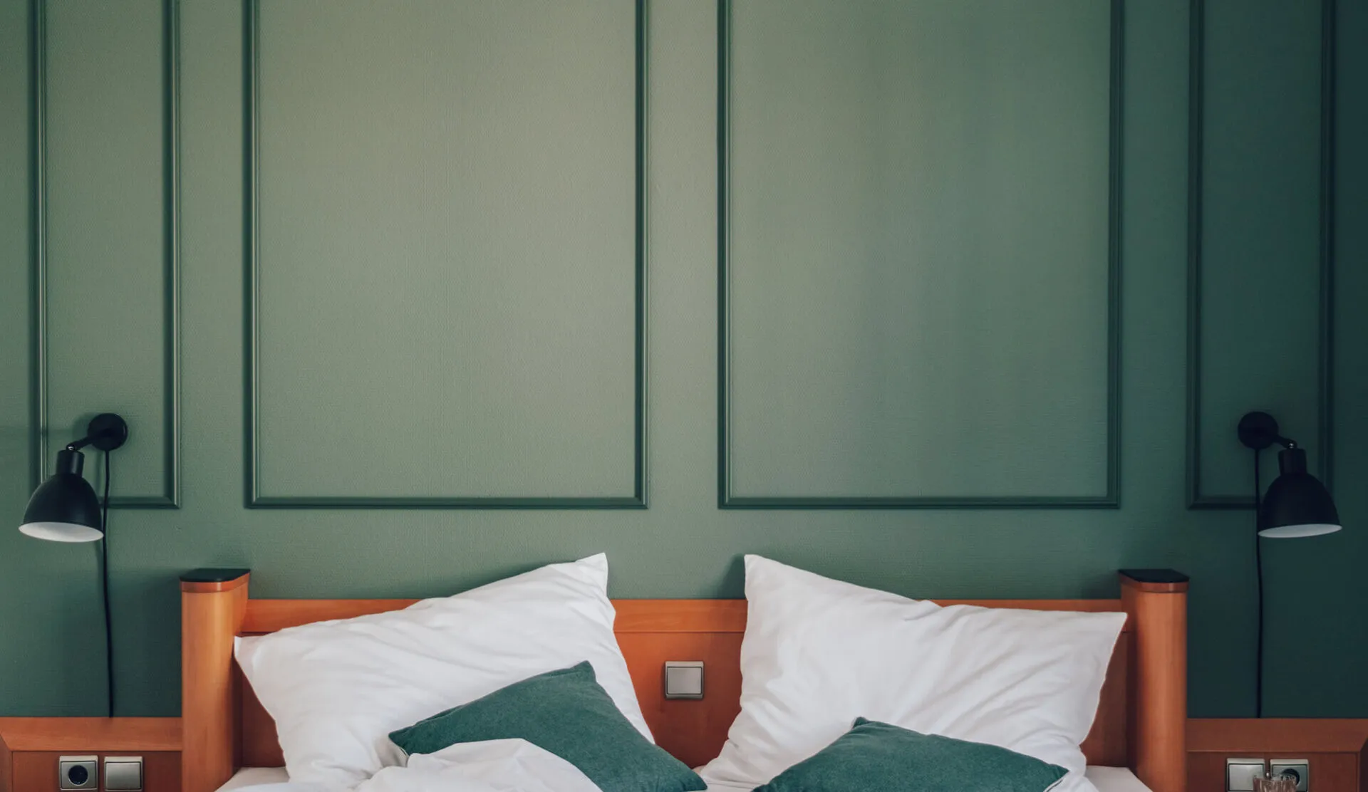 Wooden bed with white pillows in front of green wall